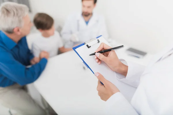 O médico de luvas brancas tira uma amostra de sangue do dedo do rapaz. Uma enfermeira está fazendo anotações no formulário . — Fotografia de Stock