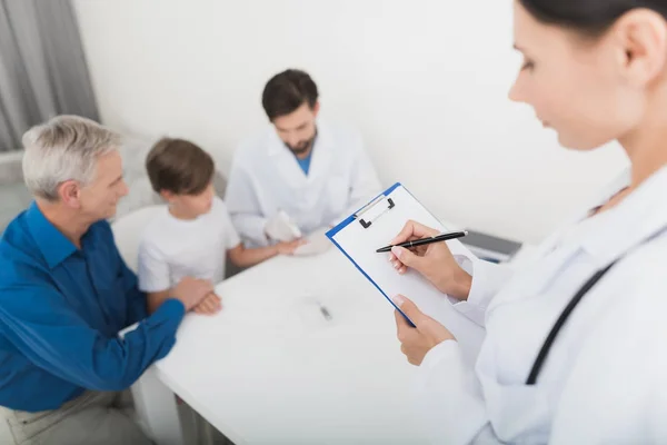 Lékaři v bílých rukavicích bere vzorek krve z prstu chlapce. Zdravotní sestra dělá poznámky na formuláři. — Stock fotografie