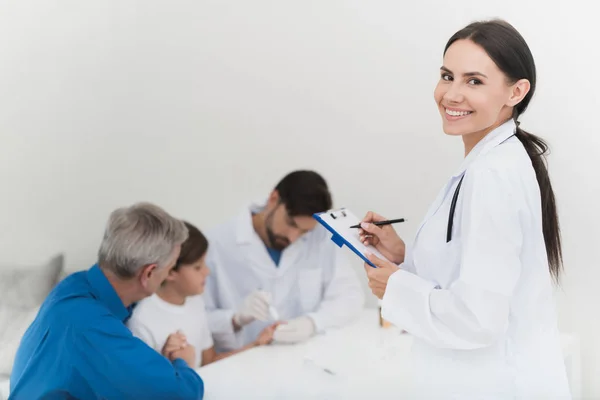 El médico con guantes blancos toma una muestra de sangre del dedo del niño. Una enfermera está tomando notas en el formulario . —  Fotos de Stock