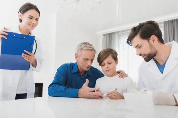 Läkaren i vita handskar tar ett blodprov från pojkens finger. Sjuksköterskan tittar på processen. — Stockfoto