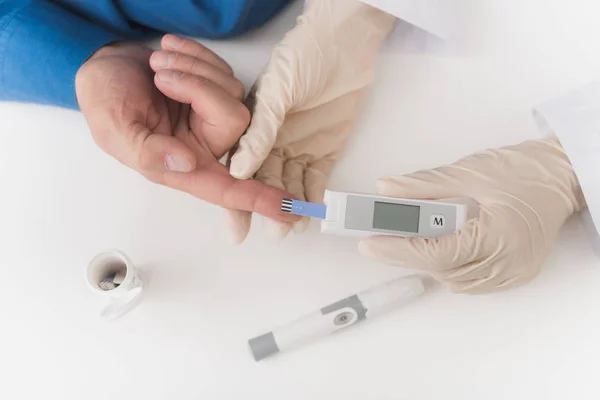 En sjuksköterska tar ett blodprov med en gammal mans Harv. Sjuksköterskan tar blodet till glycemeter. — Stockfoto