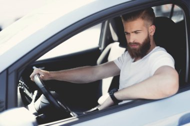 A young man with a beard sits at the wheel of an electric vehicle. clipart