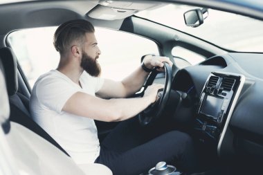 Bir sakallı bir genç adam bir elektrikli araç direksiyon başında oturur.