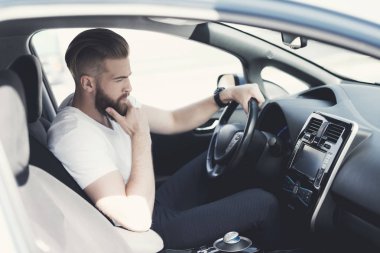 Bir sakallı bir genç adam bir elektrikli araç direksiyon başında oturur.