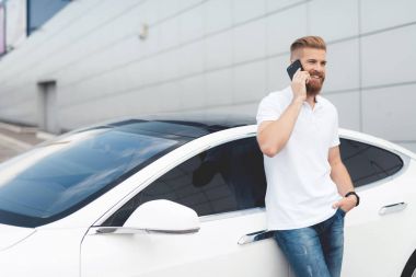 Onun elektrikli otomobil yakınındaki telefonda konuşurken sakallı genç bir adam.