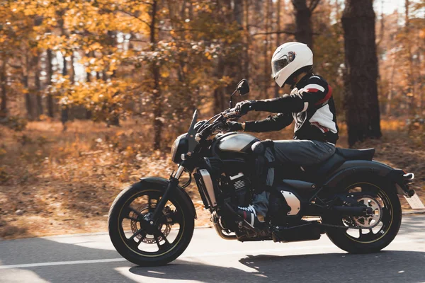 Un jeune homme avec un casque roule sur une route forestière sur une moto électrique . — Photo