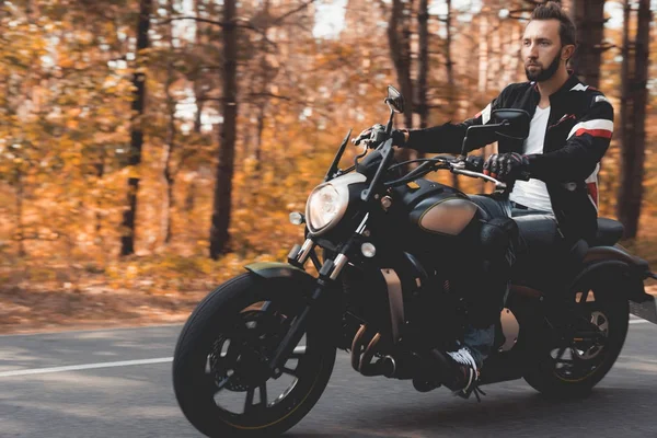 Młody facet z brodą jest jazda na leśnej drodze na motocykl elektryczny. — Zdjęcie stockowe