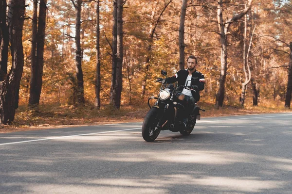 Un jeune homme barbu roule sur une route forestière sur une moto électrique . — Photo