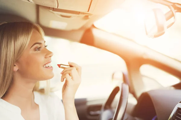 Una joven se pinta los labios mientras está sentada al volante de un coche eléctrico . —  Fotos de Stock