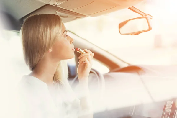 Una joven se pinta los labios mientras está sentada al volante de un coche eléctrico . — Foto de Stock