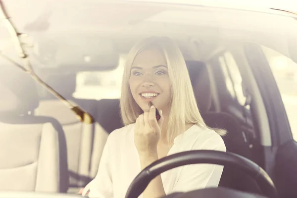 Una joven se pinta los labios mientras está sentada al volante de un coche eléctrico . —  Fotos de Stock