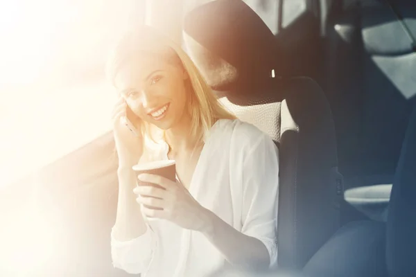 Une blonde boit du café et parle au téléphone dans une borne de recharge . — Photo