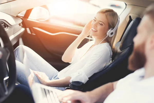 La chica escucha música en los auriculares mientras se sienta en el salón de un coche eléctrico . — Foto de Stock