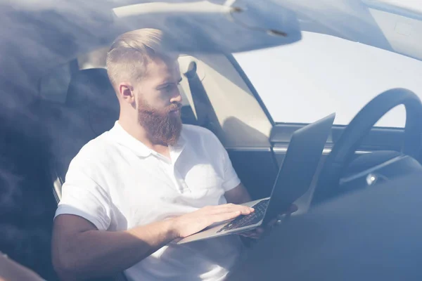 A young man with a beard sits at the wheel of an electric vehicle.