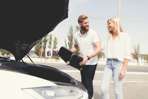 Un joven y una chica ponen equipaje en el maletero de su coche eléctrico . —  Fotos de Stock