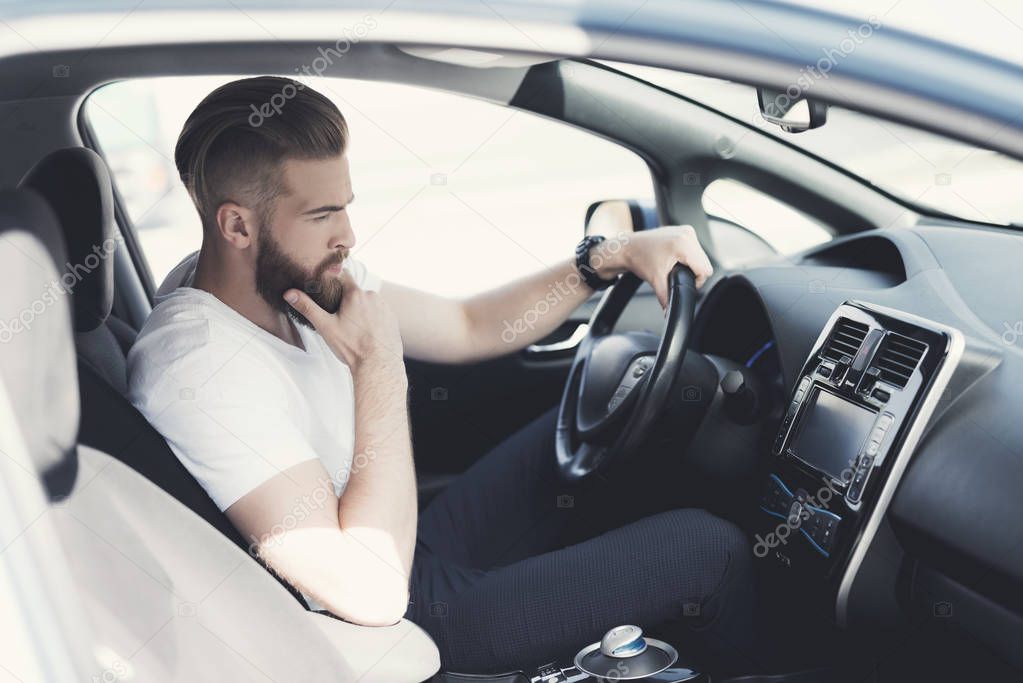 A young man with a beard sits at the wheel of an electric vehicle.