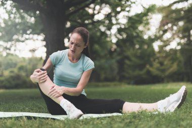 Bir kadın için yoga parkta bir halı üzerinde oturuyor. O meşgul oldu ve bacağını travma.