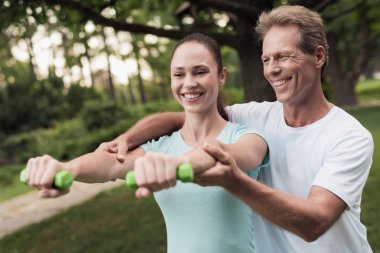 Kız parkta dumbbells ile yapıyor. Bir adam ona yardımcı olur. Onlar gülüyor