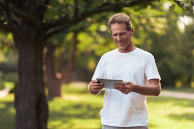 Bir parkta elinde duran gri bir tablet ile bir adam. O tablet ekranında görünüyor