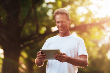 Bir parkta elinde duran gri bir tablet ile bir adam. O tablet ekranında görünüyor