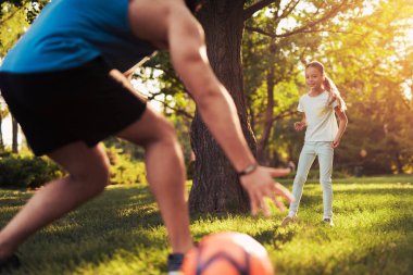 Bir kız babasıyla birlikte parkta futbol oynar. Babası kaleci rol oynamaktadır