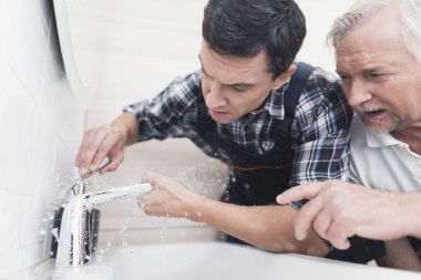 İki su tesisatçıları banyo musluk tamir. Onlardan biri dokunun yerini alan ikincisi junior öğretir.