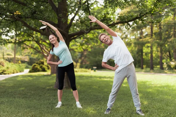 Mężczyzna i kobieta robi ćwiczenia w parku. One się rozgrzać. Stanowią one stoków — Zdjęcie stockowe
