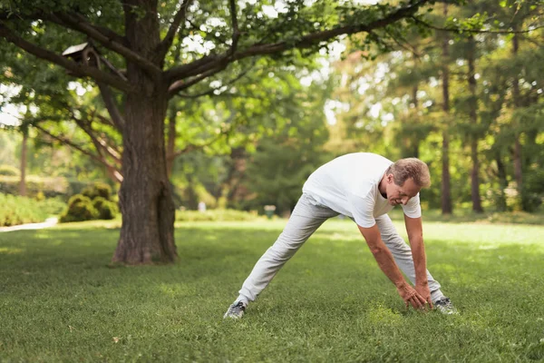 Um homem de sportswear leve está fazendo exercícios no parque — Fotografia de Stock