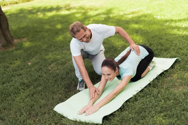 Woman doing warm-up on a rug for yoga, a man helping her — Stock Photo, Image