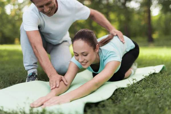 Жінка робить розминку на килимку для йоги, чоловік допомагає їй — стокове фото