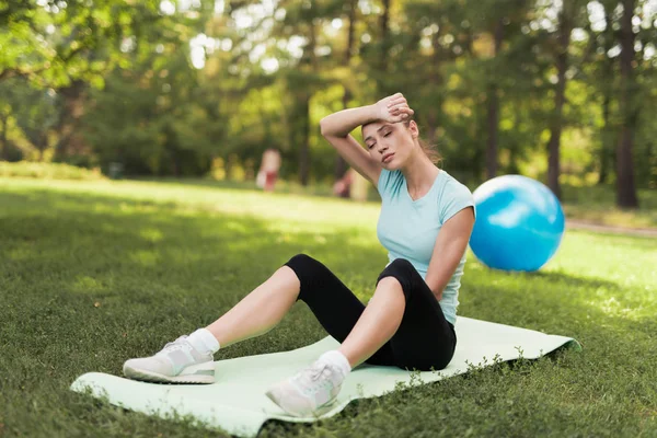 Eine Frau sitzt auf einem Teppich für Yoga und ruht sich nach dem Training aus. Hinter ihr liegt ein blauer Ball für Yoga. — Stockfoto