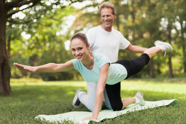 Ein Paar treibt Sport in einem warmen Sommerpark. ein Mann hilft einer Frau zu dehnen. — Stockfoto