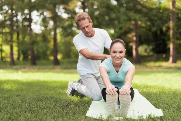 Ein Mann hilft einer Frau, sich zu dehnen. sie sitzt auf einem Teppich für Yoga — Stockfoto