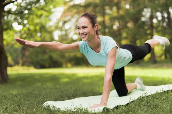 Une fille fait des étirements sur un tapis pour le yoga dans le parc. Elle sourit. . — Photo