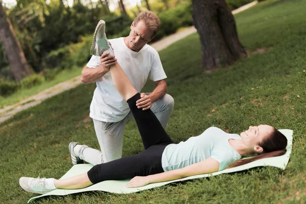 Ein Mann hilft seinem Mädchen beim Stretching. sie liegt auf einem Teppich für Yoga, ein Mann hält ihr Bein — Stockfoto