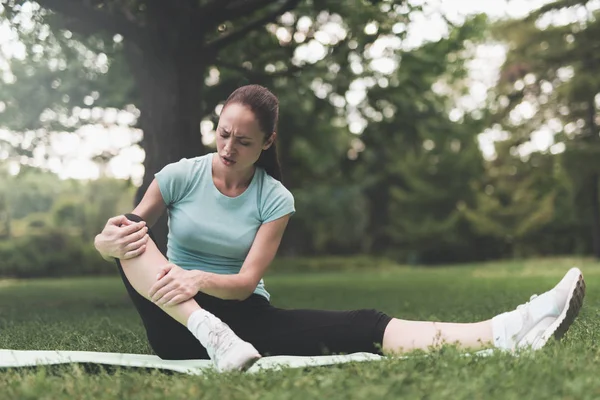 Bir kadın için yoga parkta bir halı üzerinde oturuyor. O meşgul oldu ve bacağını travma.