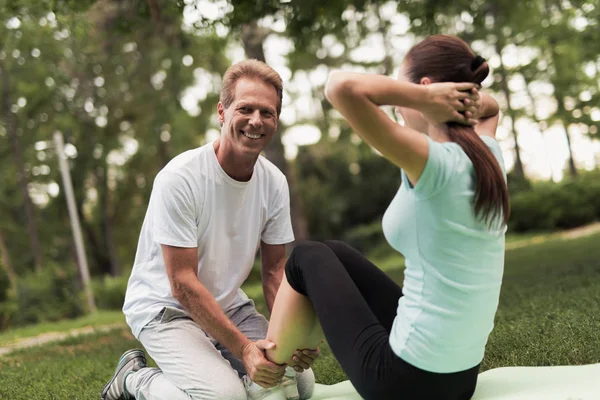 Eine Frau erschüttert die Presse über die Natur. Sie sitzt auf einem Teppich für Yoga. ein Mann hilft ihr und hält ihre Beine. — Stockfoto