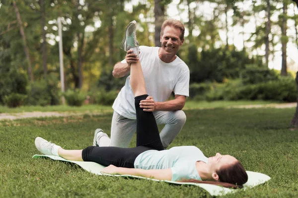 Ein Mann hilft seinem Mädchen beim Stretching. sie liegt auf einem Teppich für Yoga, ein Mann hält ihr Bein — Stockfoto