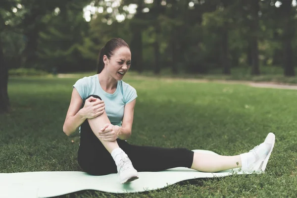 A woman is sitting on a rug for yoga in the park. She was engaged and traumatized her leg. — Stock Photo, Image