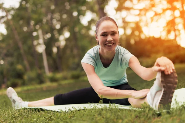 Женщина делает растяжку на ковре для йоги в парке. Она тянет себя к ногам — стоковое фото