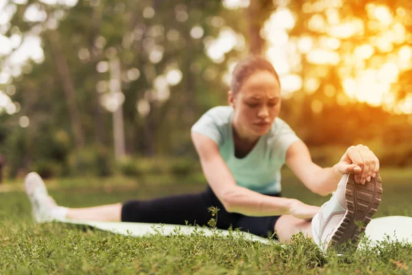 Женщина делает растяжку на ковре для йоги в парке. Она тянет себя к ногам — стоковое фото