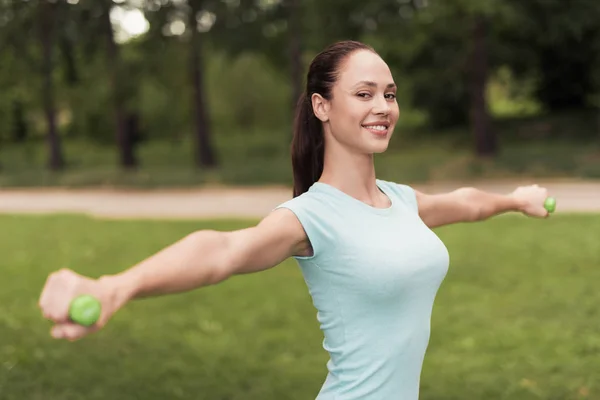 Pige i parken laver øvelser med håndvægte - Stock-foto