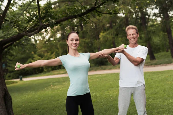 Kız parkta dumbbells ile yapıyor. Bir adam ona yardımcı olur. Onlar gülüyor
