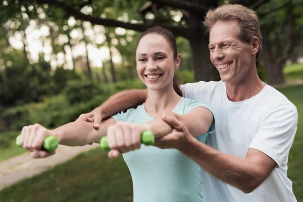 Kız parkta dumbbells ile yapıyor. Bir adam ona yardımcı olur. Onlar gülüyor