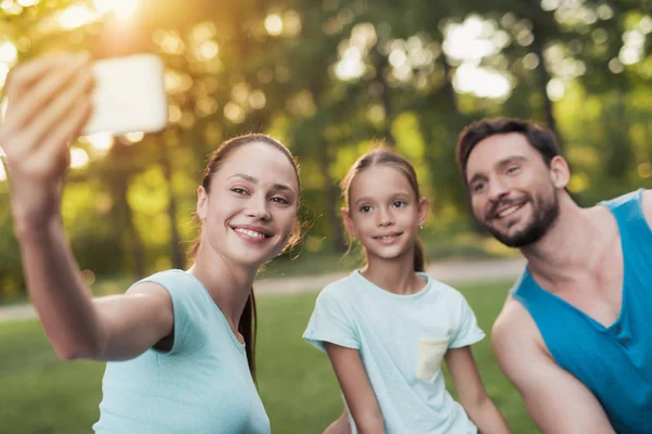 La familia descansa en el parque después de practicar deportes. Una mujer hace selfie con su familia — Foto de Stock