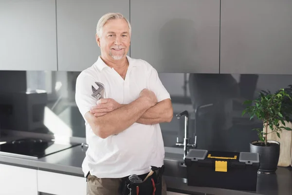 El hombre está en la cocina. Tiene una llave de cromo en la mano. Junto a él hay una caja de herramientas . — Foto de Stock