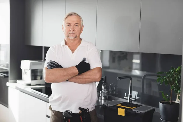 El hombre está en la cocina. Tiene guantes negros de trabajo en las manos. Junto a él hay una caja de herramientas . — Foto de Stock