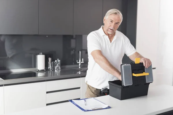 El hombre está en la cocina. Saca herramientas para trabajos de reparación de su caja de herramientas negra . — Foto de Stock