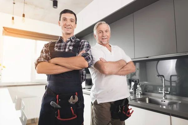 Dos plomeros masculinos posando en una cocina moderna. Tienen un uniforme especial, junto a ellos una caja negra para el instrumento . — Foto de Stock