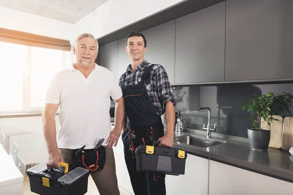 Dos hombres de plomeros se paran en la cocina y posan con cajas de herramientas negras . — Foto de Stock